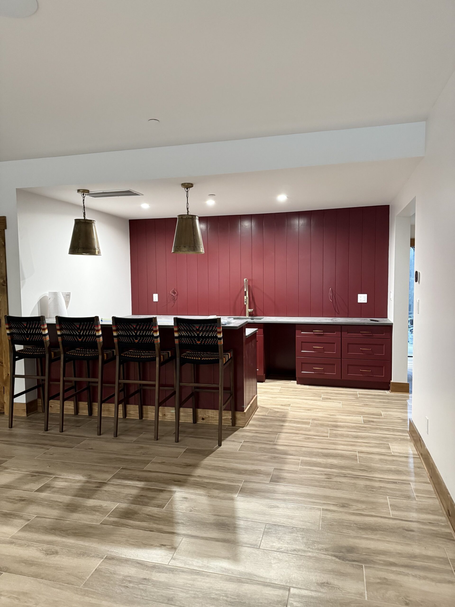 Custom burgundy bar cabinetry with brass pendant lighting and wood-look tile flooring, finished by L&J Painting Group