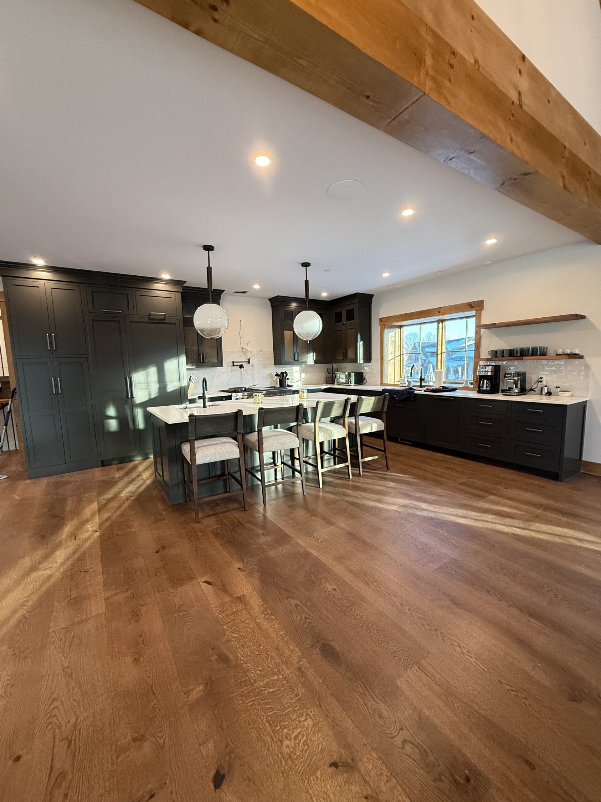 Custom charcoal shaker kitchen with reclaimed wood beam, brass pendant lighting, and waterside view, finished by L&J Painting Group