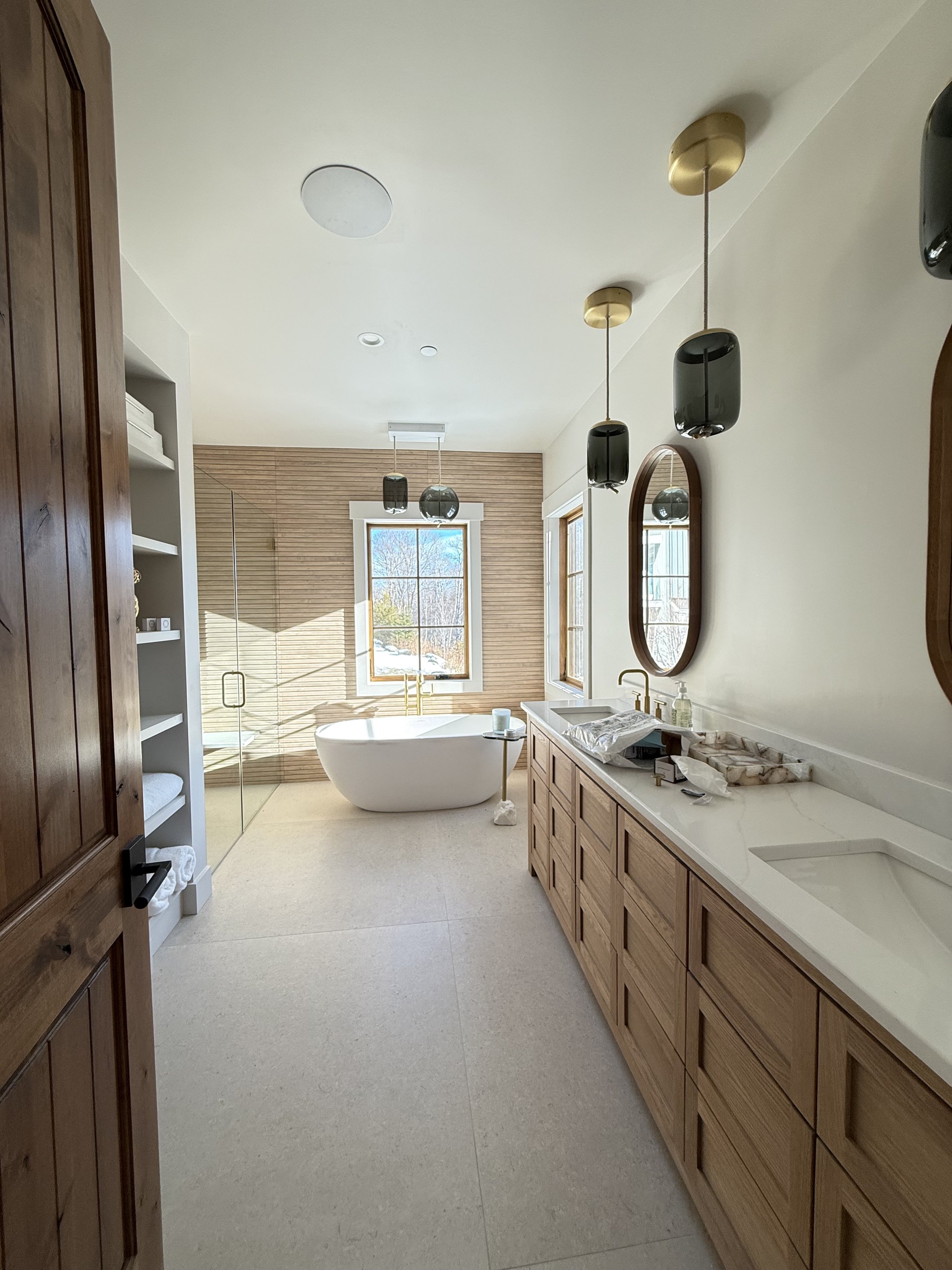 Primary bath with freestanding tub, wood-slat accent wall, and dual vanity with brass fixtures, finished by L&J Painting Group