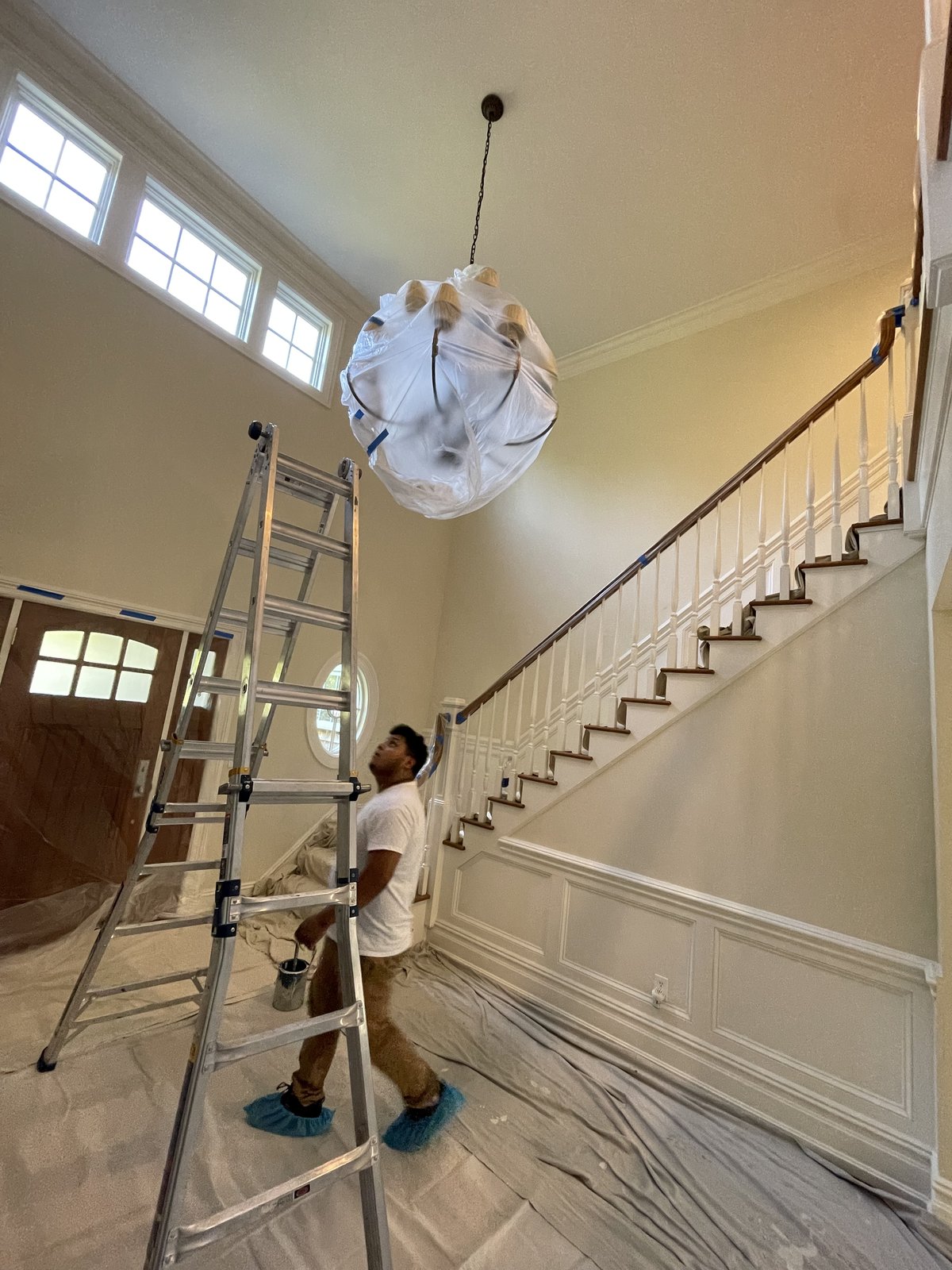 L&J Painting Group crew member painting a two-story foyer near a chandelier