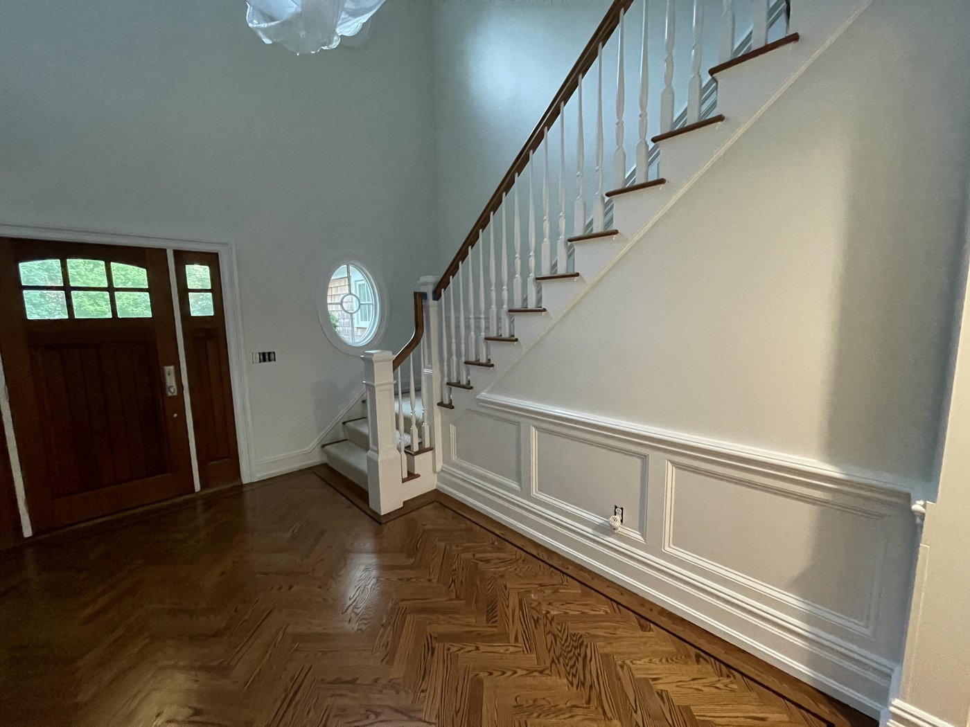 Grand entry foyer with herringbone hardwood floors, curved staircase, and paneled wainscoting, finished by L&J Painting Group