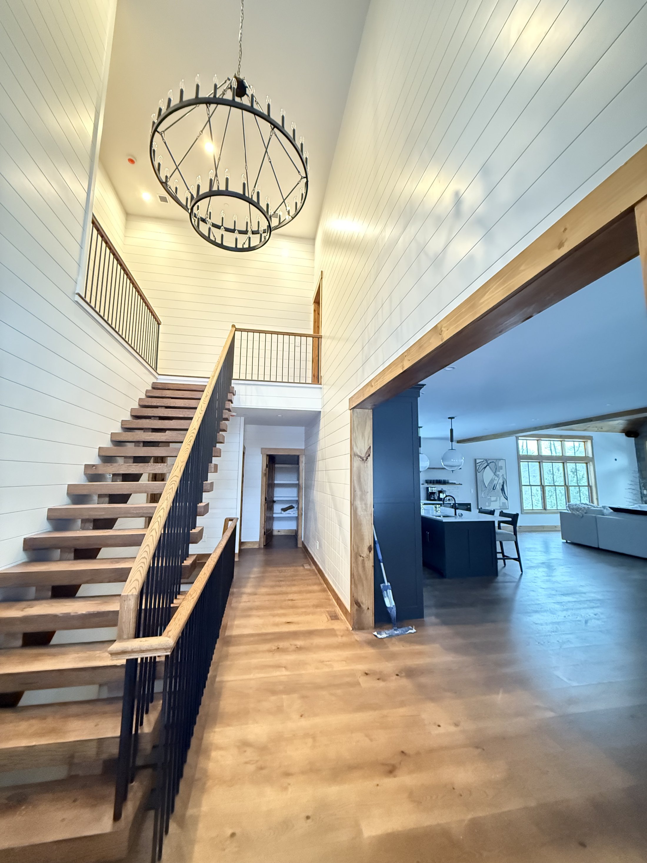 Vaulted staircase landing with statement chandelier and open-concept kitchen beyond, finished by L&J Painting Group