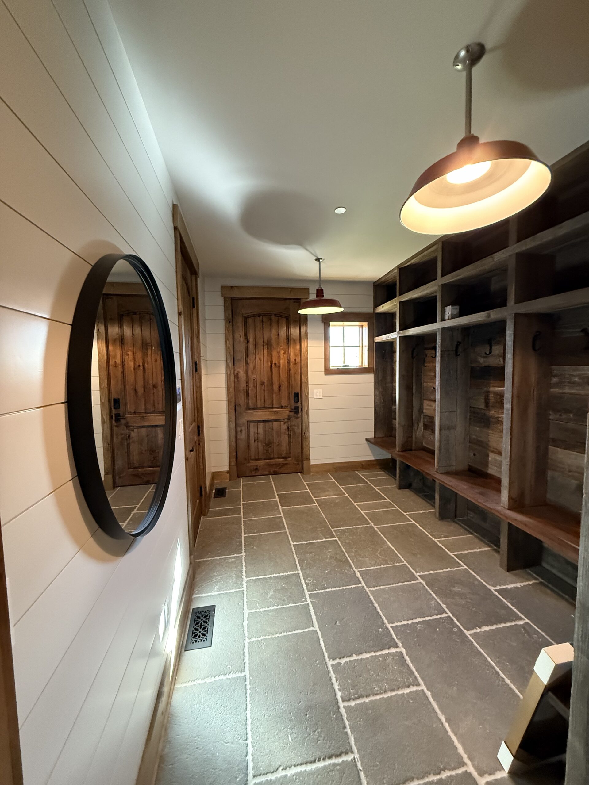Custom mudroom with reclaimed wood built-in lockers, stone tile floor, and warm barn-style lighting, finished by L&J Painting Group
