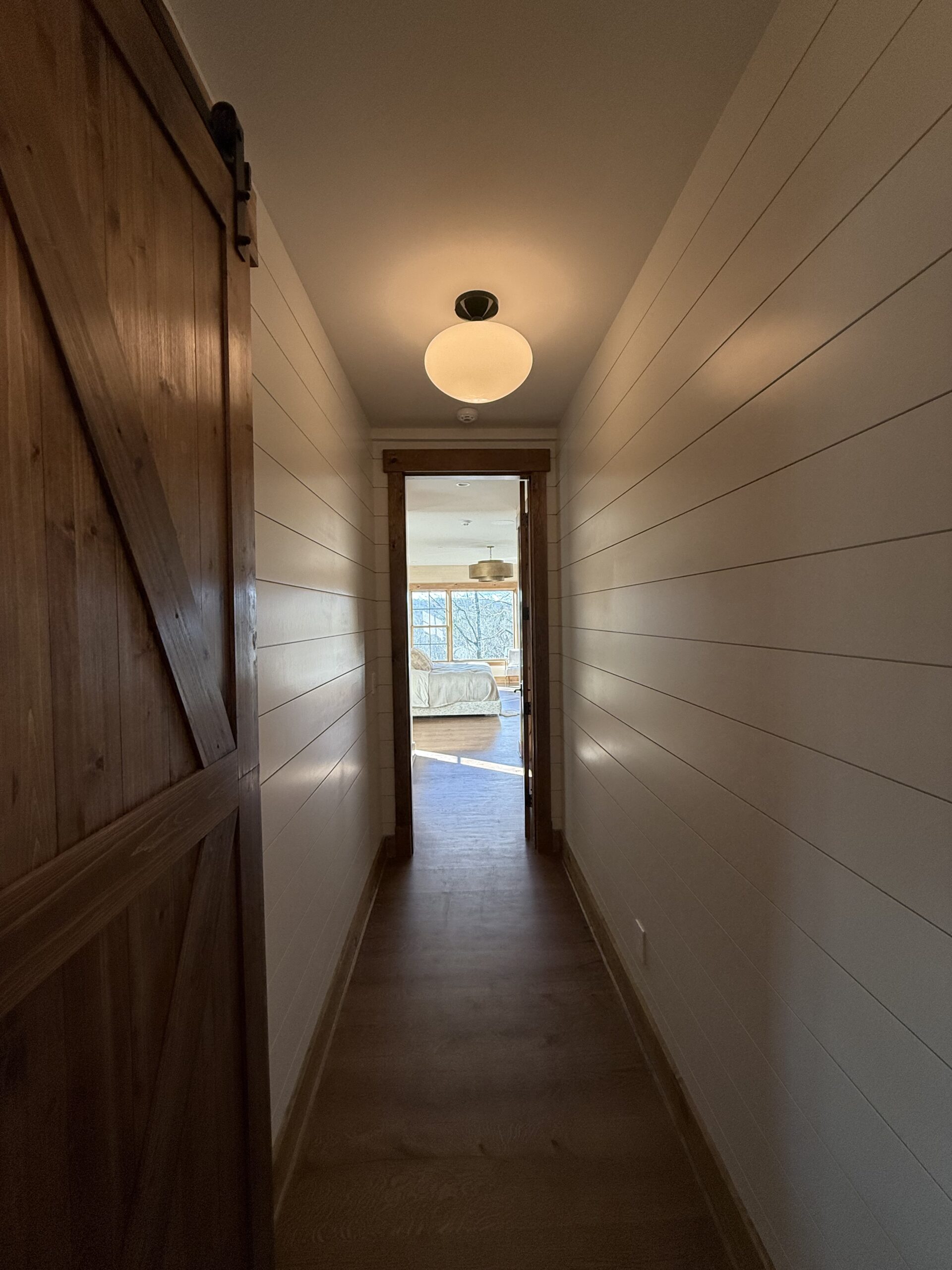 Shiplap hallway with barn door and warm globe pendant lighting, finished by L&J Painting Group