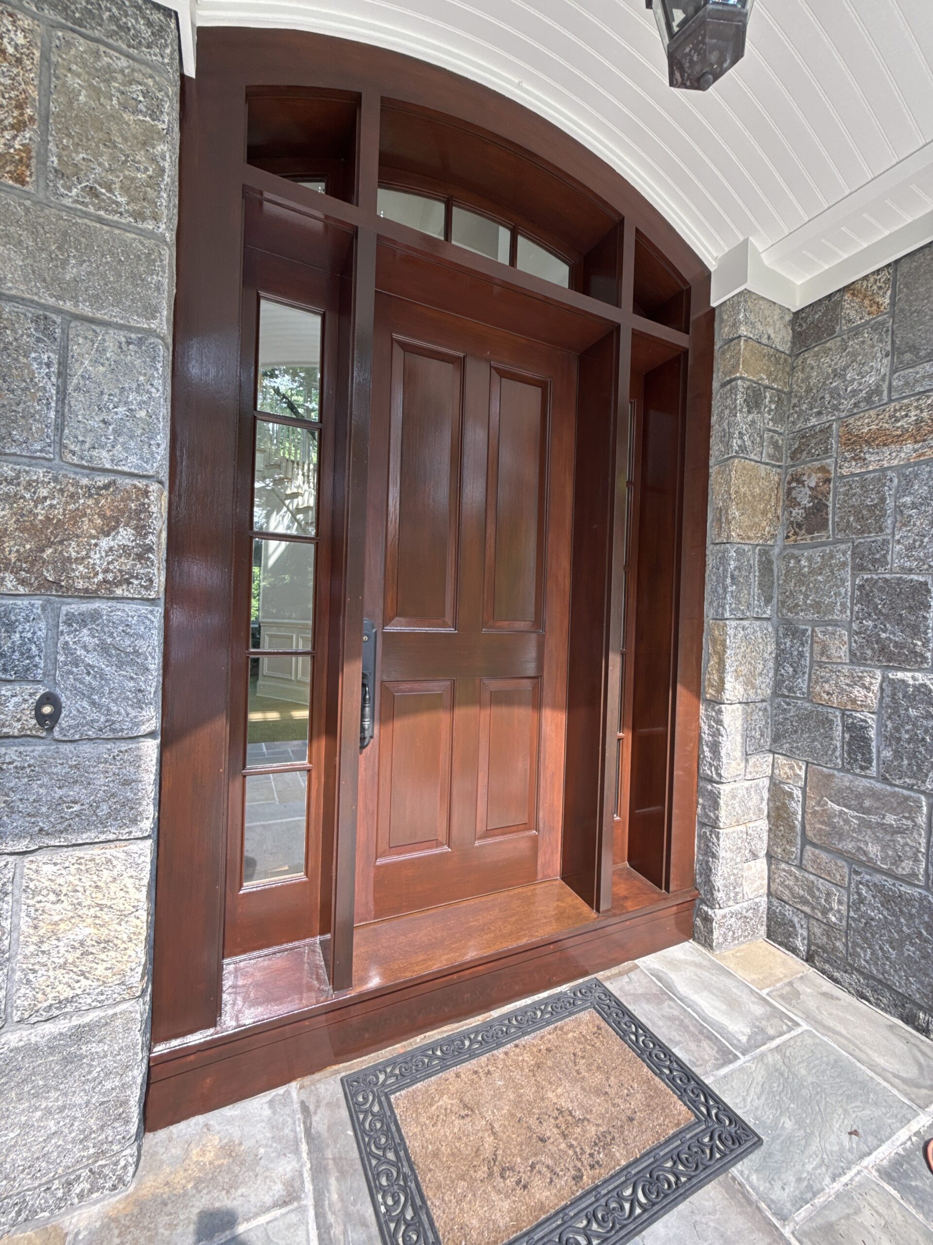 Finished mahogany-stained front entry door with a stone surround, by L&J Painting Group