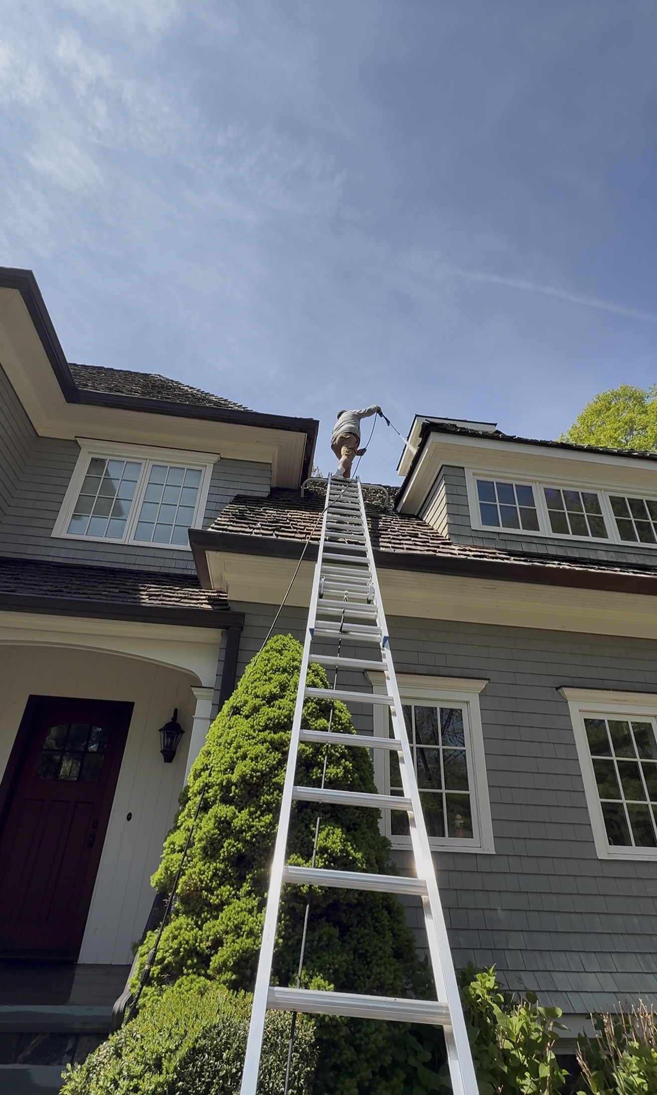 Power washing technician cleaning the roofline of a premium shingle-style home with a red front door, Fairfield County CT
