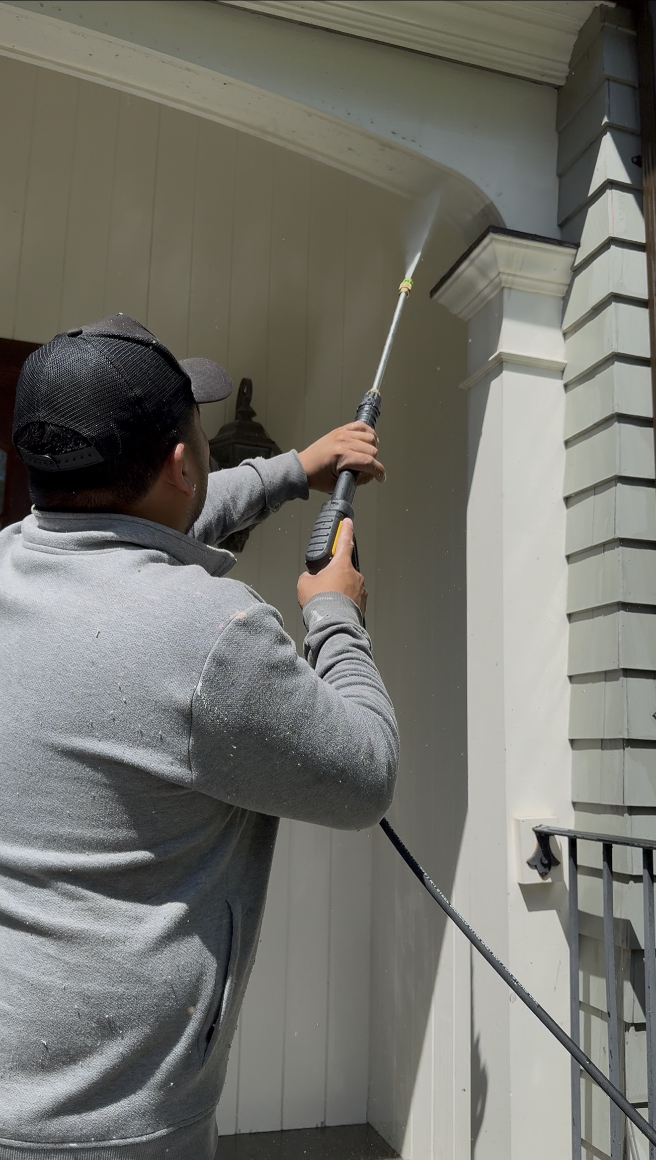 L&J technician power washing a porch column and archway with a pressure wand, close-up technique
